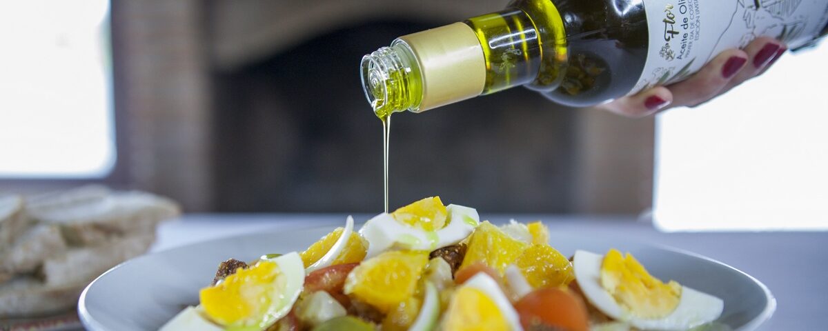 Mano de una mujer vertiendo aceite de oliva virgen extra Flor de Oro sobre una ensalada.